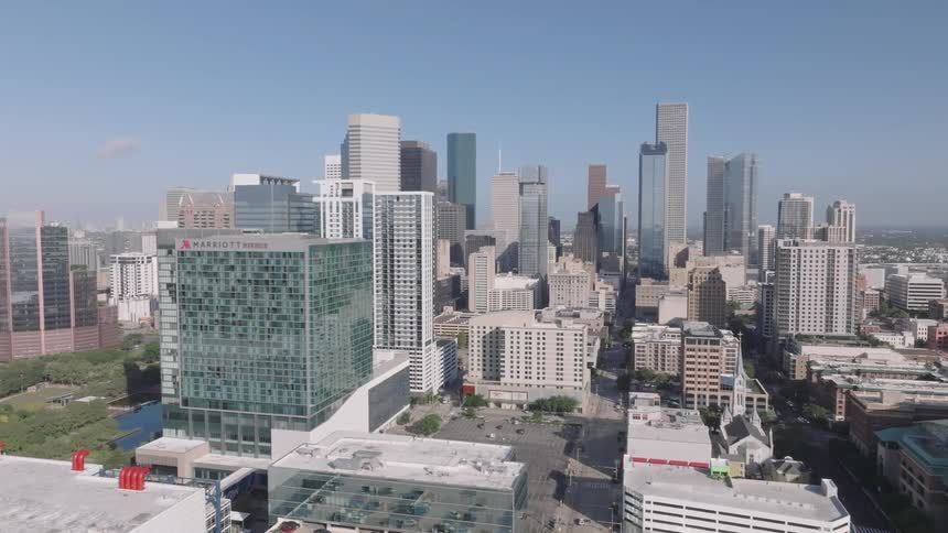 An aerial shot pans slowly across the downtown skyline of a large city on a clear day the city is filled with many tall skyscrapers and other buildings and a large marriott marquis hotel is prominent in the foreground