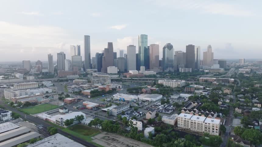 An aerial shot captures a busy highway with multiple lanes of traffic leading into a large city skyline on a cloudy day the camera slowly moves along the highway revealing the sprawling urban landscape
