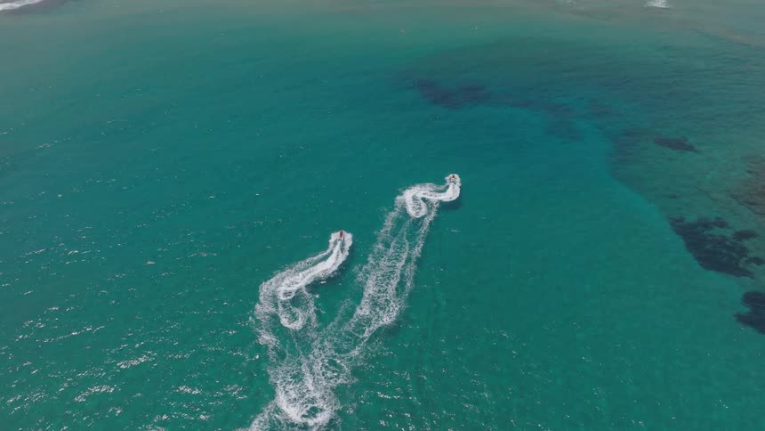 Two jet skis leaving white trails as they glide across the blue sea