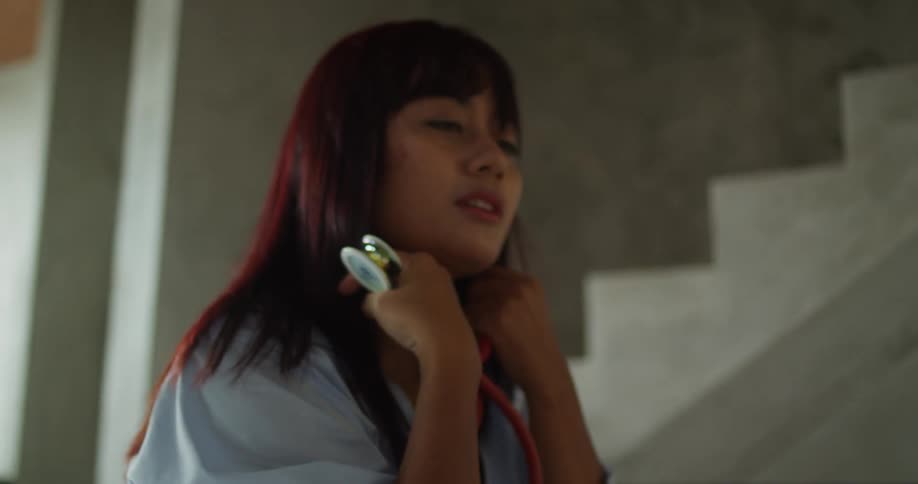 The video shows a medium closeup of a person with long dark hair wearing a light blue shirt a red stethoscope is around their neck and they appear to be a doctor or medical professional