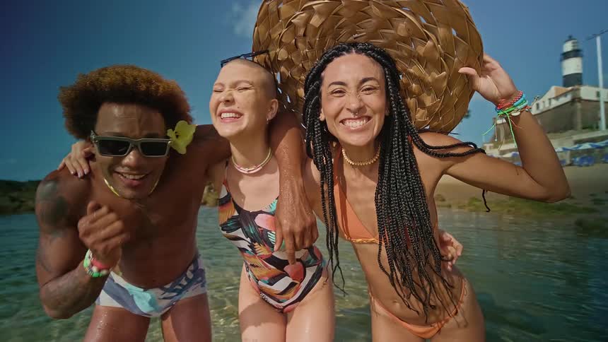 Three people standing in the water smiling and laughing at the camera