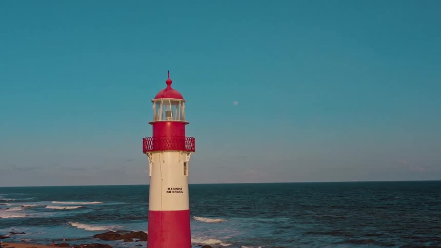 A lighthouse on the shoreline at sunset with ocean waves hitting the shore