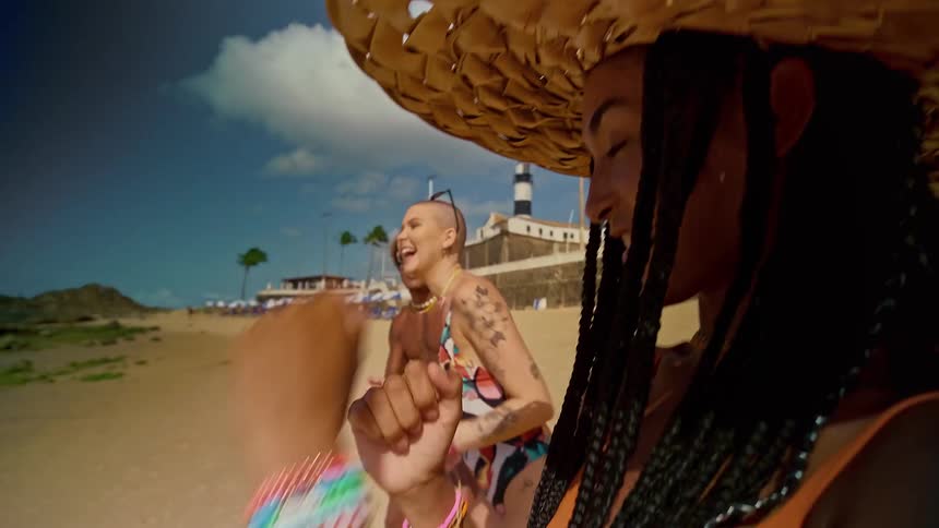 Three touristsa man and two womendancing and excited on the beach sand on a sunny day all smiling with one woman wearing a sun hat over her braided hair