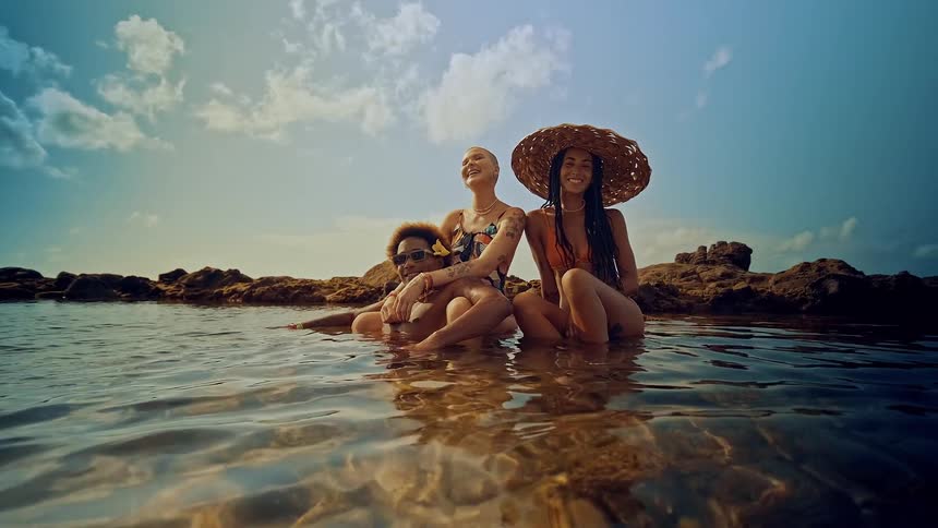 Three people sitting on a rock in the middle of the sea smiling