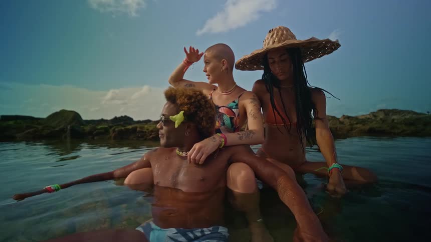 Two women and a man sitting in the water at the beach with the man leaning intimately against one of the women