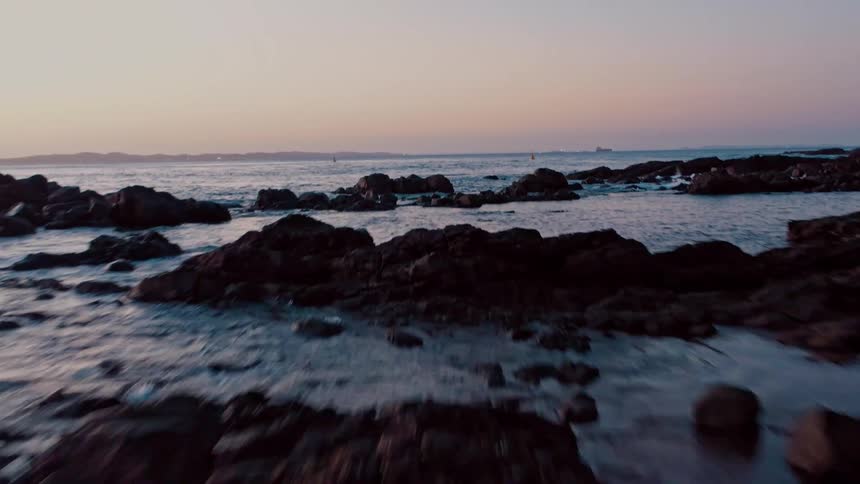 Coastal rocks with gentle waves at sunset under a sky in shades of pink and blue
