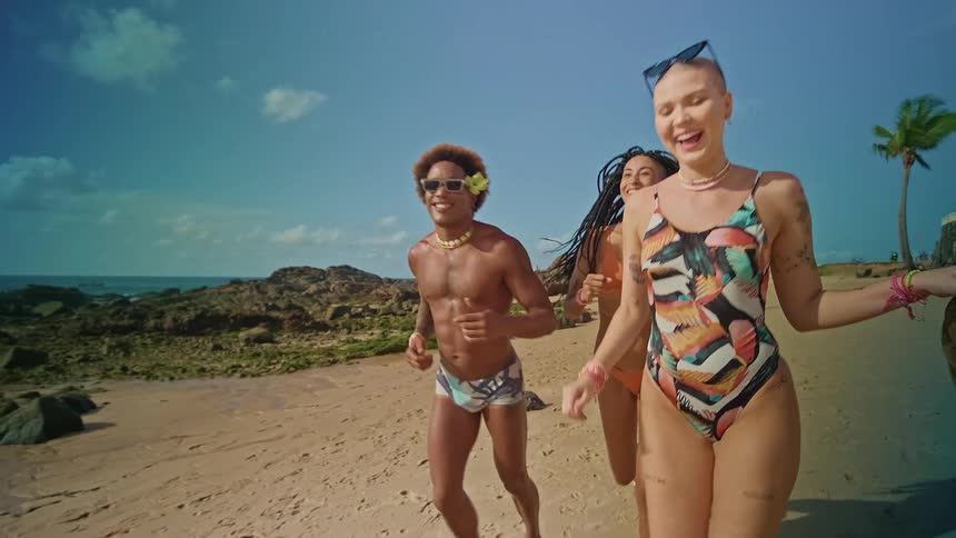 Three young adult friends run across the beach outdoors during daytime