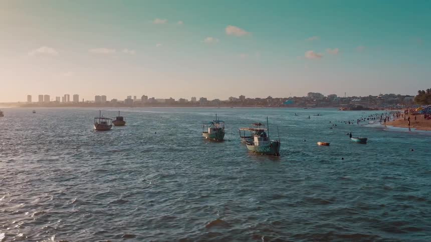 Fishing boats float near a coastal city under a clear blue sky