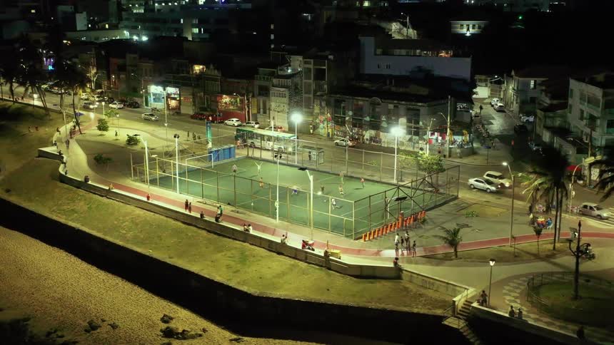 A group of people playing soccer on a field beside a busy road in the city at night