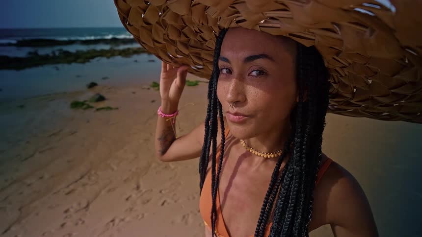 The woman wearing a straw hat is walking on the beach