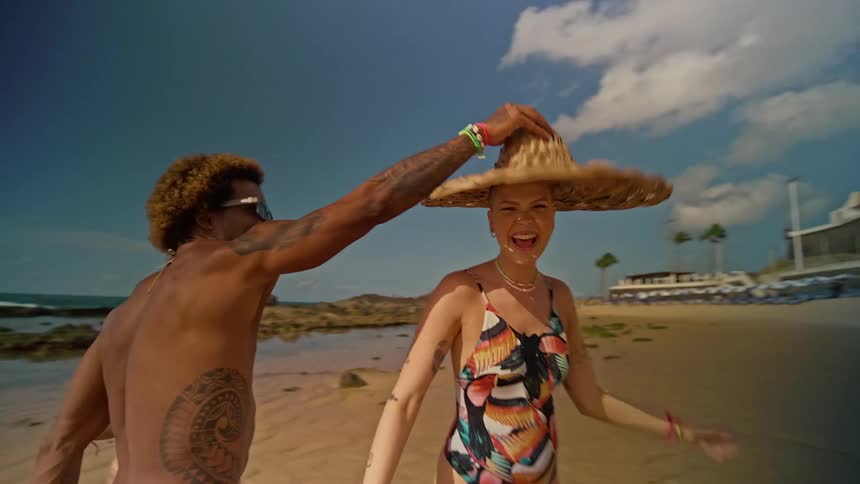 Three friends having fun on a beach with one of them putting a hat on another