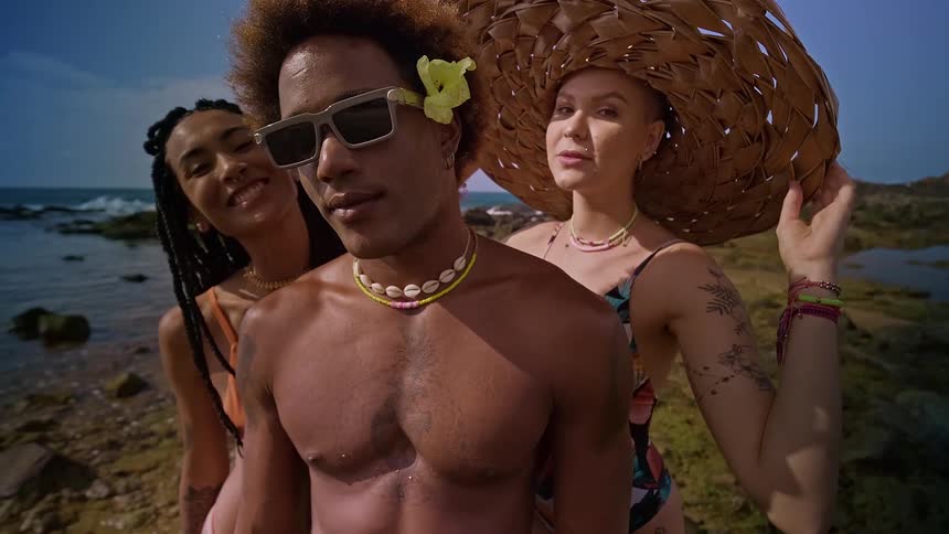 Two women and a man in beachwear posing at the edge of the beach