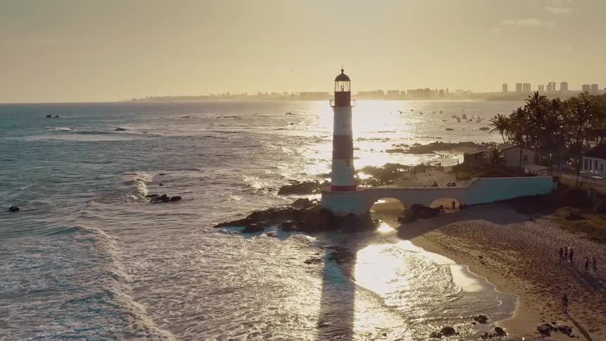 Lighthouse by the sea casting a shadow on the beach at sunset