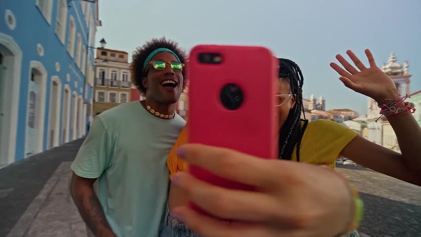 A group of three young friends is taking a selfie with a red phone they are all smiling and making fun poses enjoying their time together outdoors