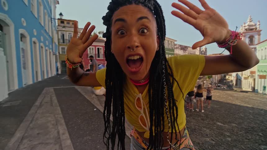 Woman opens her mouth in surprise with her back to a crowd of people on the cobblestone street