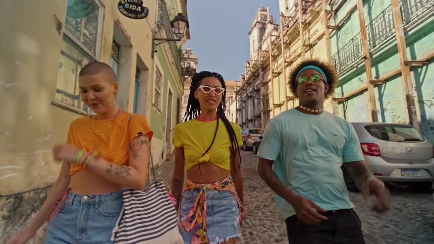 Three young people walk smiling along a cobblestone street in a historic center