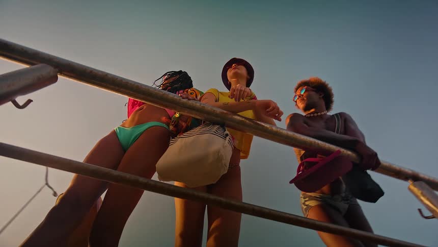 A lowangle shot captures three people standing on a boat deck looking up at the sky they are all wearing swimsuits and sunglasses and they appear to be enjoying a sunny day