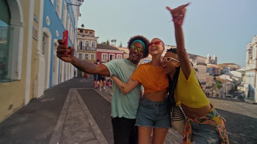 Three tourists smiling and posing together for a selfie two women and one man