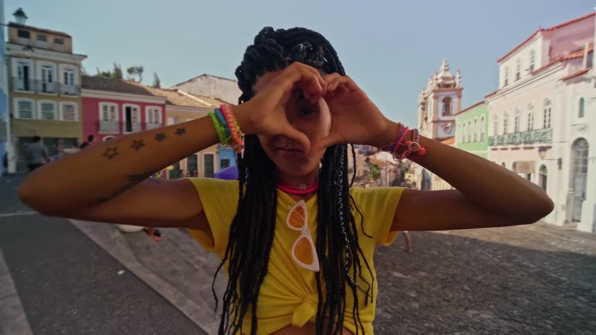 Portrait of a young woman making a heart sign with her hands while standing outdoors on a city street during daytime