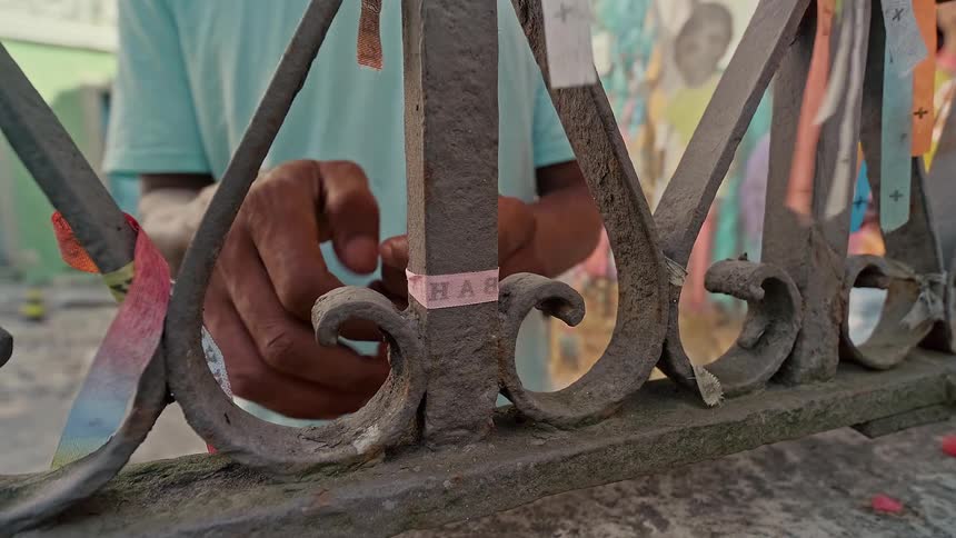 A man tying a piece of cloth to a railing fence at midday in the city