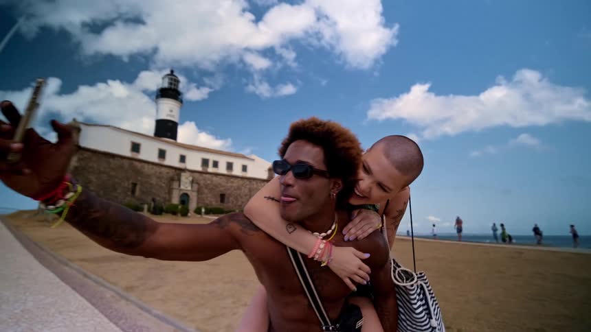 Woman clinging to a mans shoulders taking a photo in a touristy seaside setting