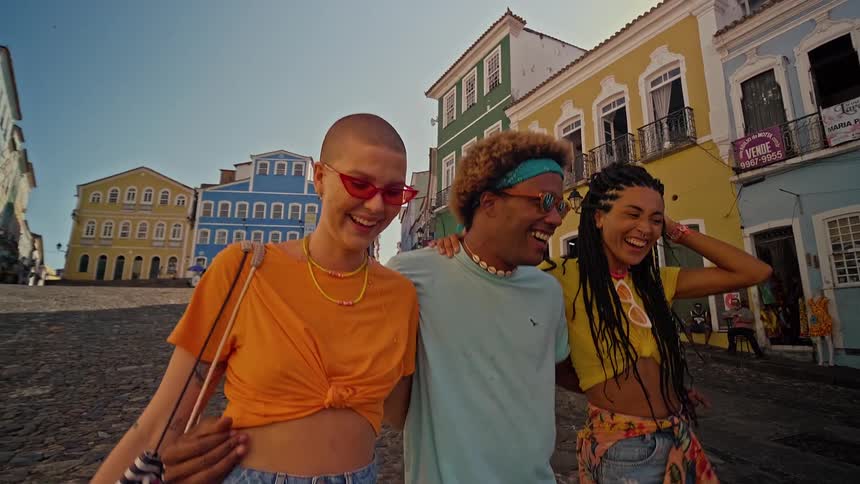A man walks with his arms around two women through a quaint area with multiple colorful buildings