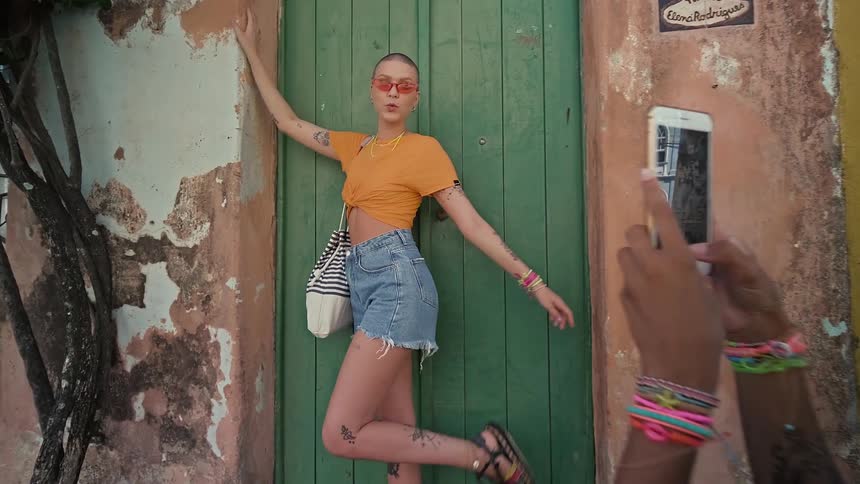 Person poses for a photo in front of a green door while another takes the picture with a phone