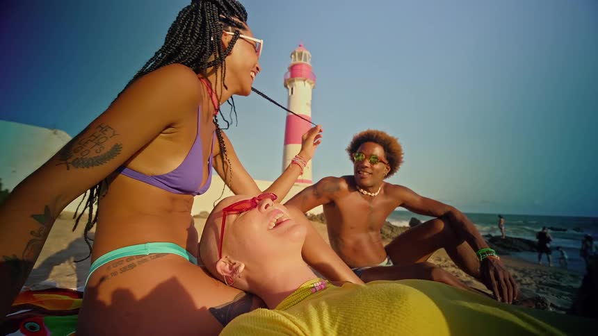 Two women and a man sitting on the sand at the beach talking and laughing together