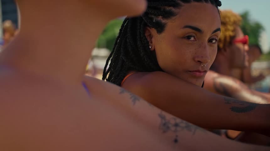 The video shows a closeup of a person with dreadlocks and a nose ring looking into the camera the persons face is partially obscured by the shoulder of another person in the foreground