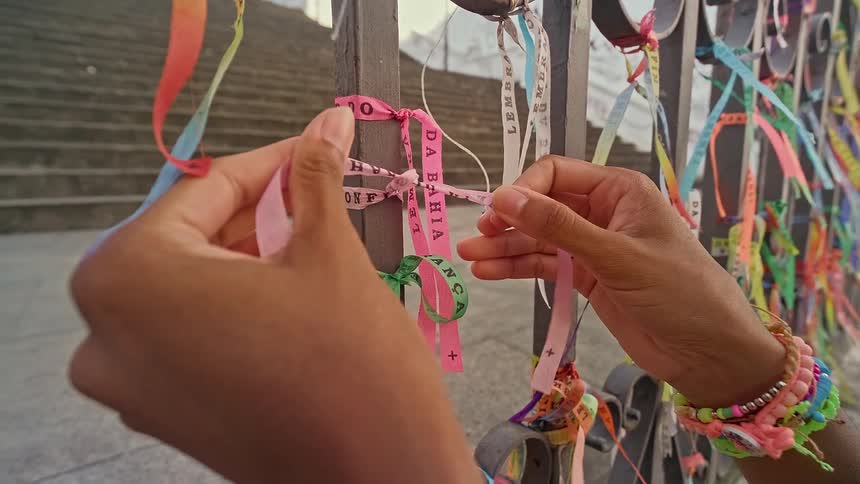 Pair of hands tying a colorful ribbon on a metal gate
