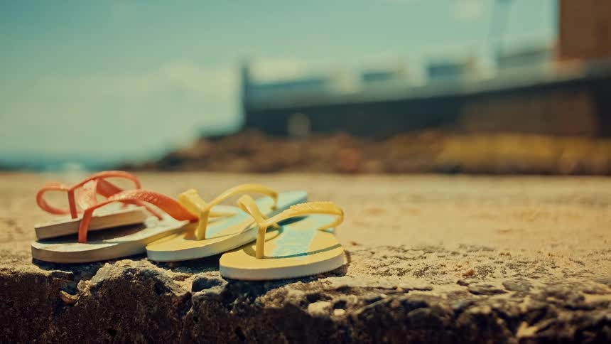 Two pairs of flipflops in an outdoor setting with the sea in the background