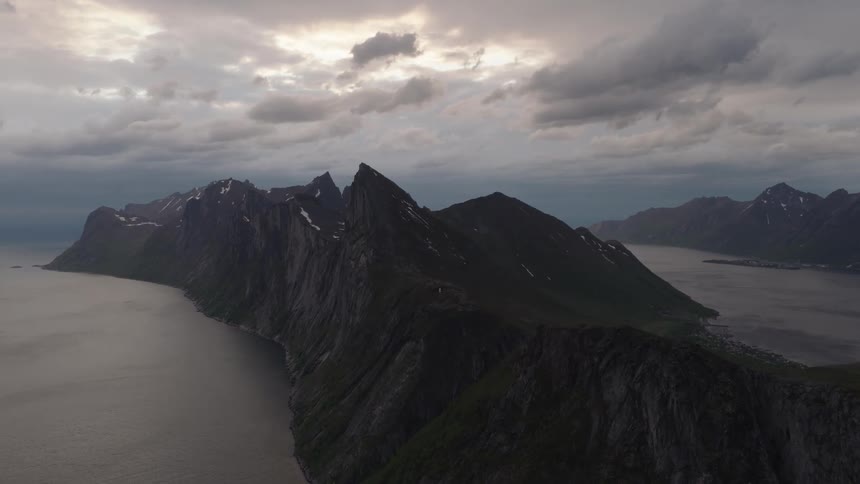A mountain stretching along the coastline surrounded by the ocean on a cloudy day