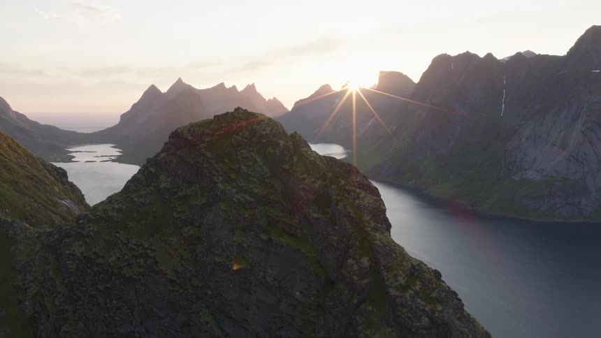 Scene of mountains surrounded by the sea and the sun on the horizon