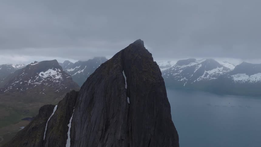 A mountain peak partly covered in snow surrounded by a series of mountains and a lake with fog covering the atmosphere
