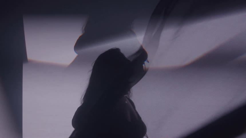 Silhouette of a woman among abstract curtains in an interior space with low lighting