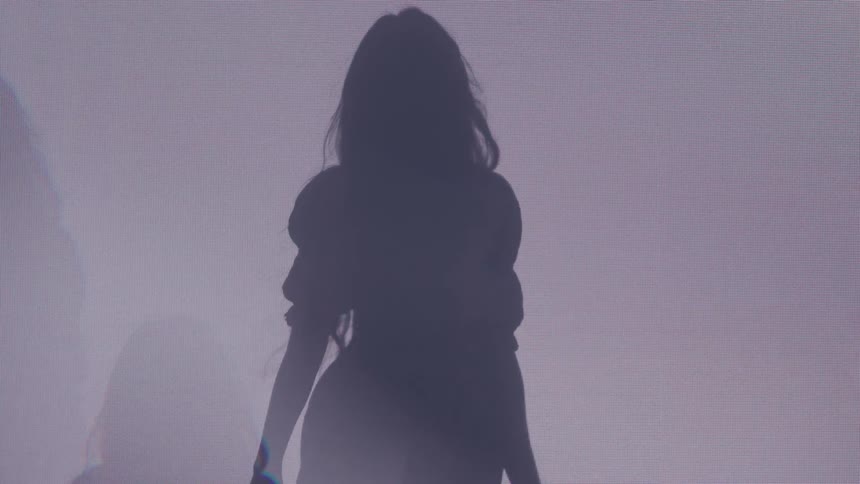 A woman with long wavy hair is shown in silhouette against a brightly lit background as she slowly turns her head and body causing her hair to flow dramatically