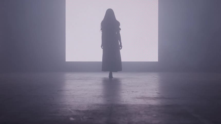 Silhouette of a woman walking in a dark room with a light in the background