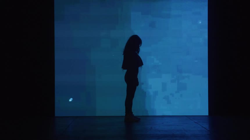The video shows a side profile of a woman silhouetted against a wall of colorchanging lights the lights cycle from green to orange and back to green