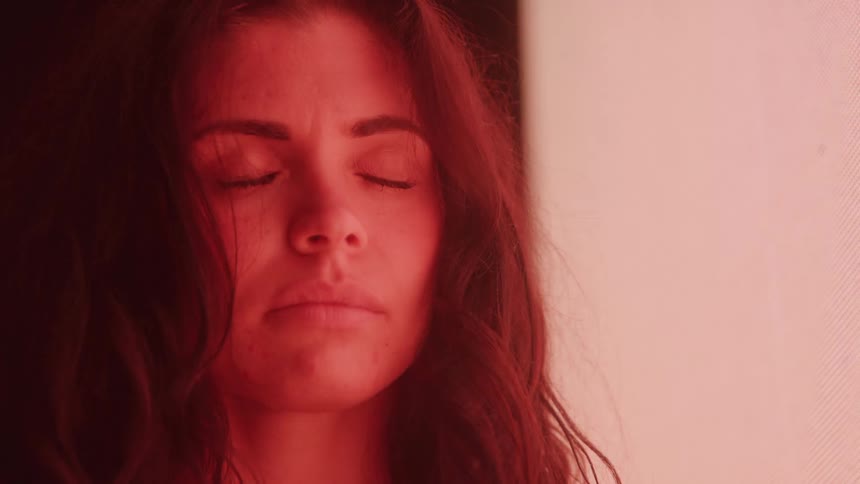 Woman with a serious expression looks upward beside a bright light