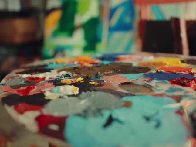 Palette with mixed paint and painted canvases in the background