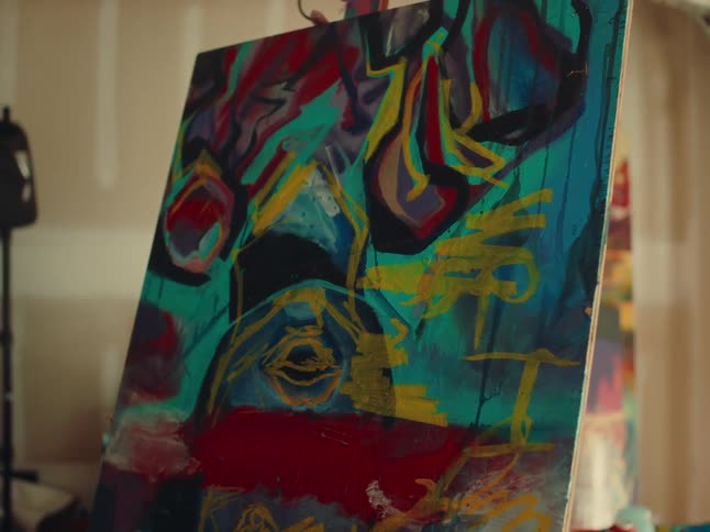 An artist painting on a canvas inside a studio at midday with the artwork featuring a series of color strokes including red blue green and yellow