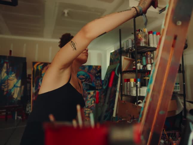 Woman sitting painting a canvas in a room with other paintings