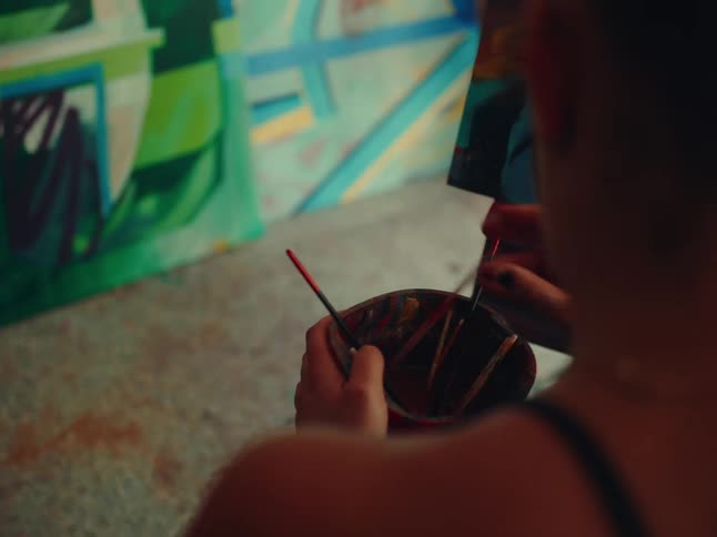 A woman washing brushes then dipping a brush in paint and painting on a canvas