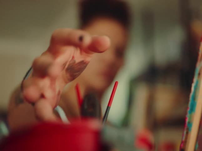 Close up of a female artist rinsing a paintbrush in a plastic container while painting a canvas in an art studio during daytime