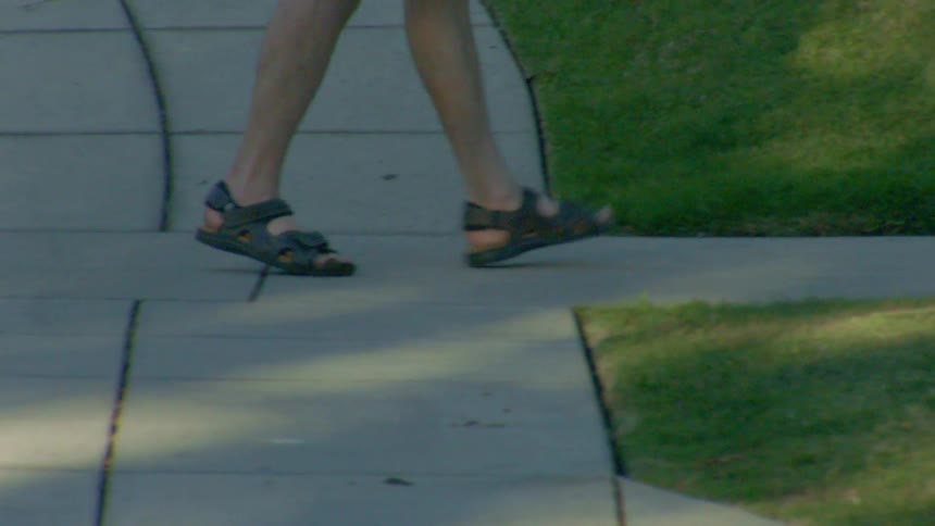 Person walking on a concrete sidewalk wearing dark sandals