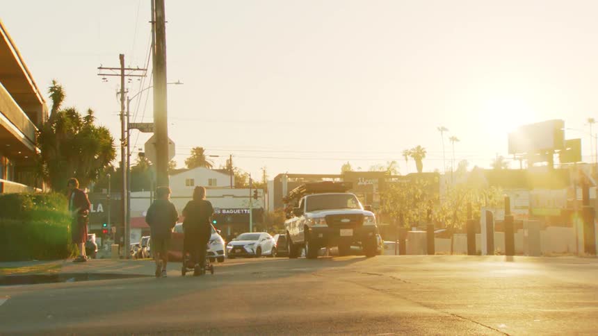 People walk across a city street at sunset in warm golden light