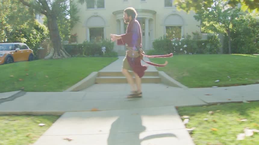 A man walks briskly on a sunny suburban sidewalk with an intense expression