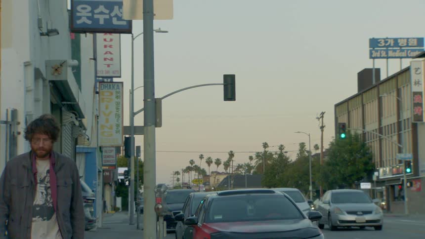 A disheveled man walks alone on a city sidewalk during golden hour