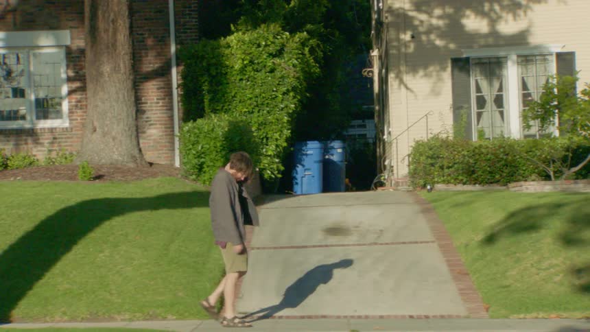 A man walking on the sidewalk under the sun in a suburban area