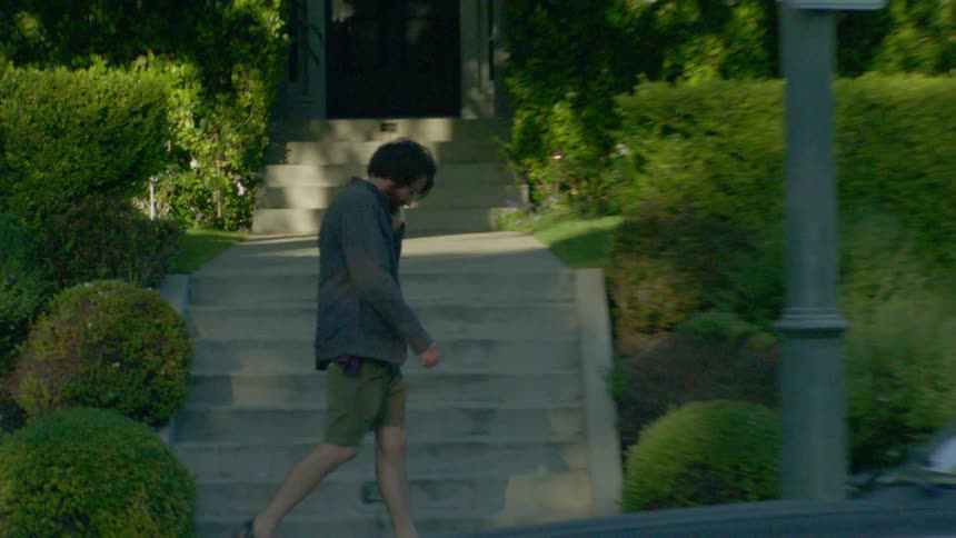 A man walks wearily along a suburban sidewalk in soft daylight